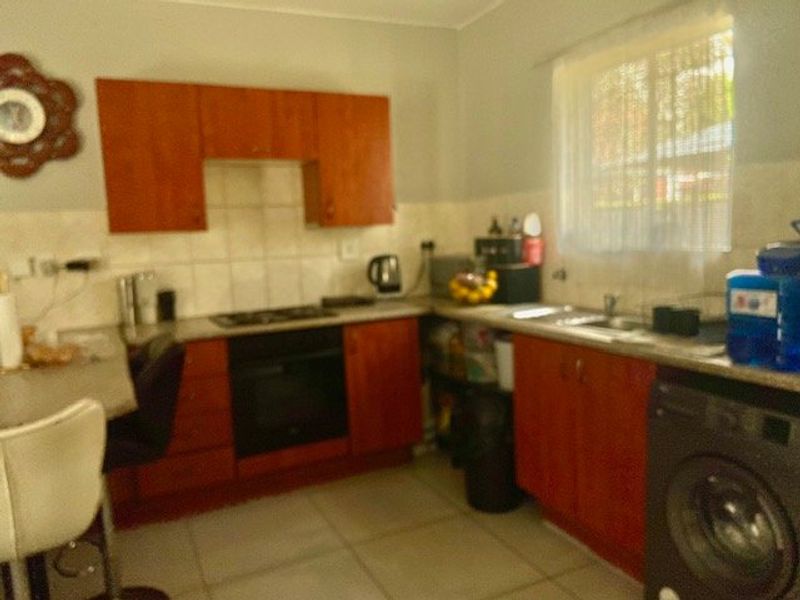 A functional kitchen featuring wooden cabinetry, tiled backsplash, built-in oven, hob, and integrated sink area with tiled flooring.
