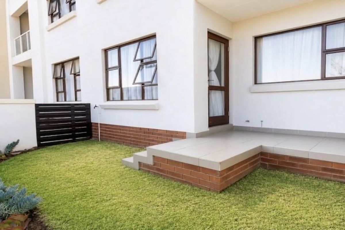 A well-maintained rear exterior view featuring a tiled patio, brick foundation, and a small private lawn area.