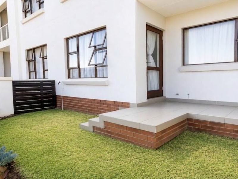 A well-maintained rear exterior view featuring a tiled patio, brick foundation, and a small private lawn area.