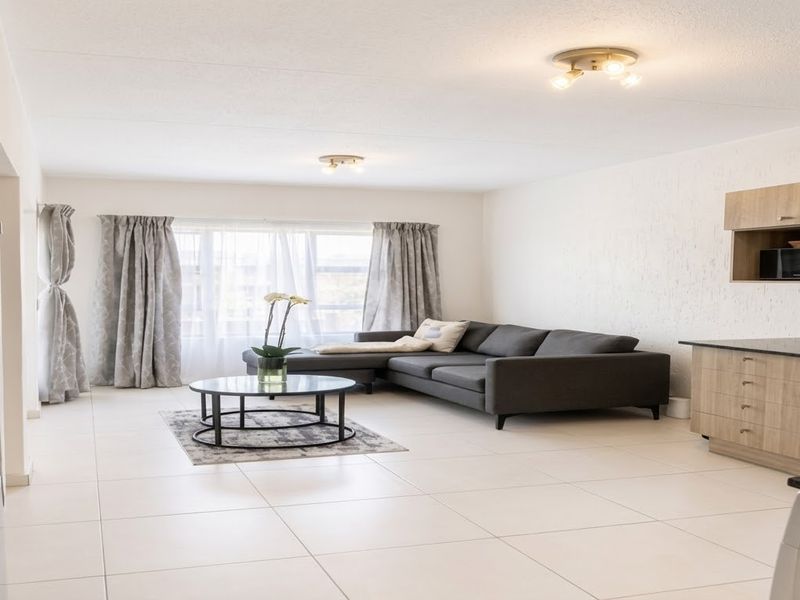 Spacious open-plan living area featuring light-toned tiled flooring and a modern kitchen with built-in cabinetry, oven, and hob.