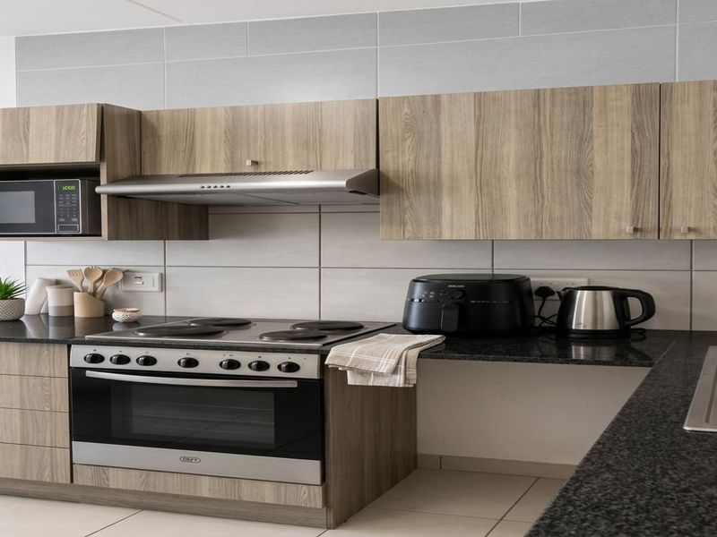 Modern kitchen featuring wood-grain cabinetry, granite countertops, stainless steel appliances, and a tiled backsplash.