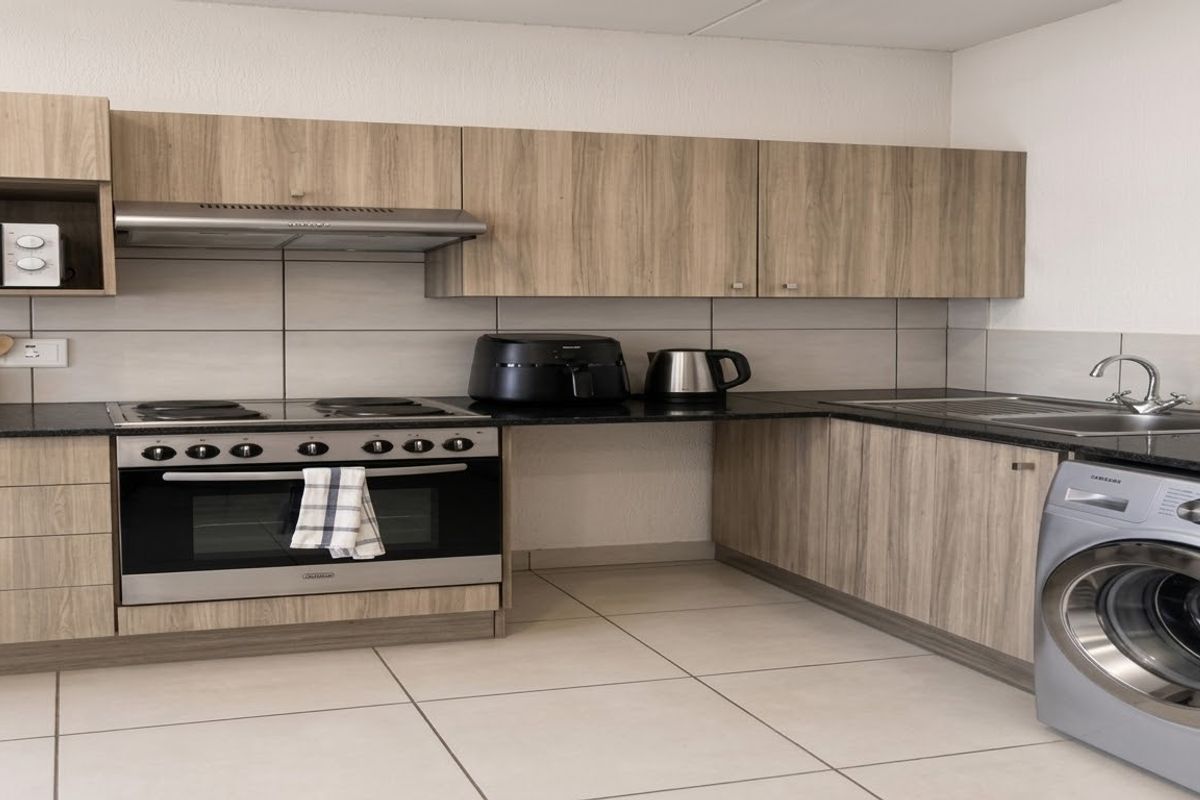 Modern kitchen featuring wood-look cabinetry, dark countertops, integrated stove with extractor, and dedicated space for laundry appliances.