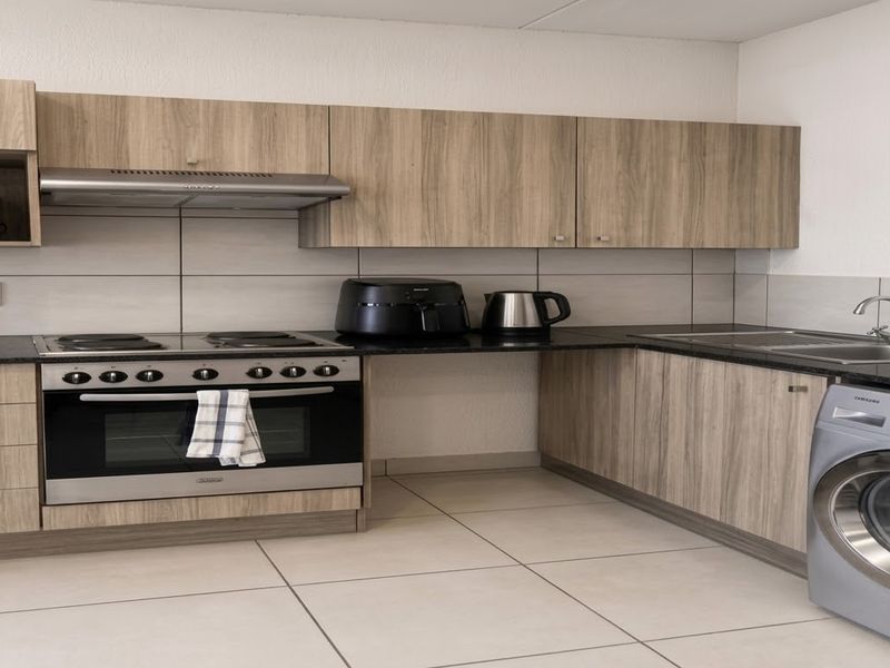 Modern kitchen featuring wood-look cabinetry, dark countertops, integrated stove with extractor, and dedicated space for laundry appliances.