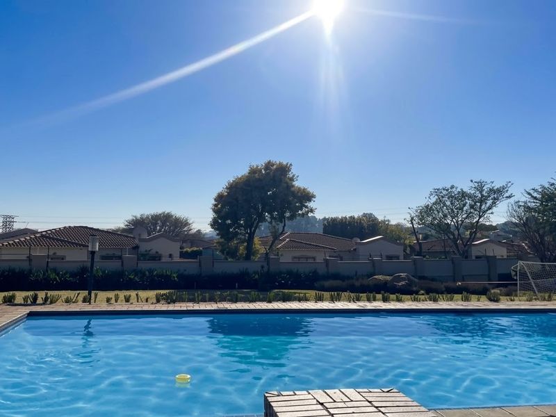 A well-maintained outdoor swimming pool area featuring brick paving and a clear view of the surrounding residential neighborhood.