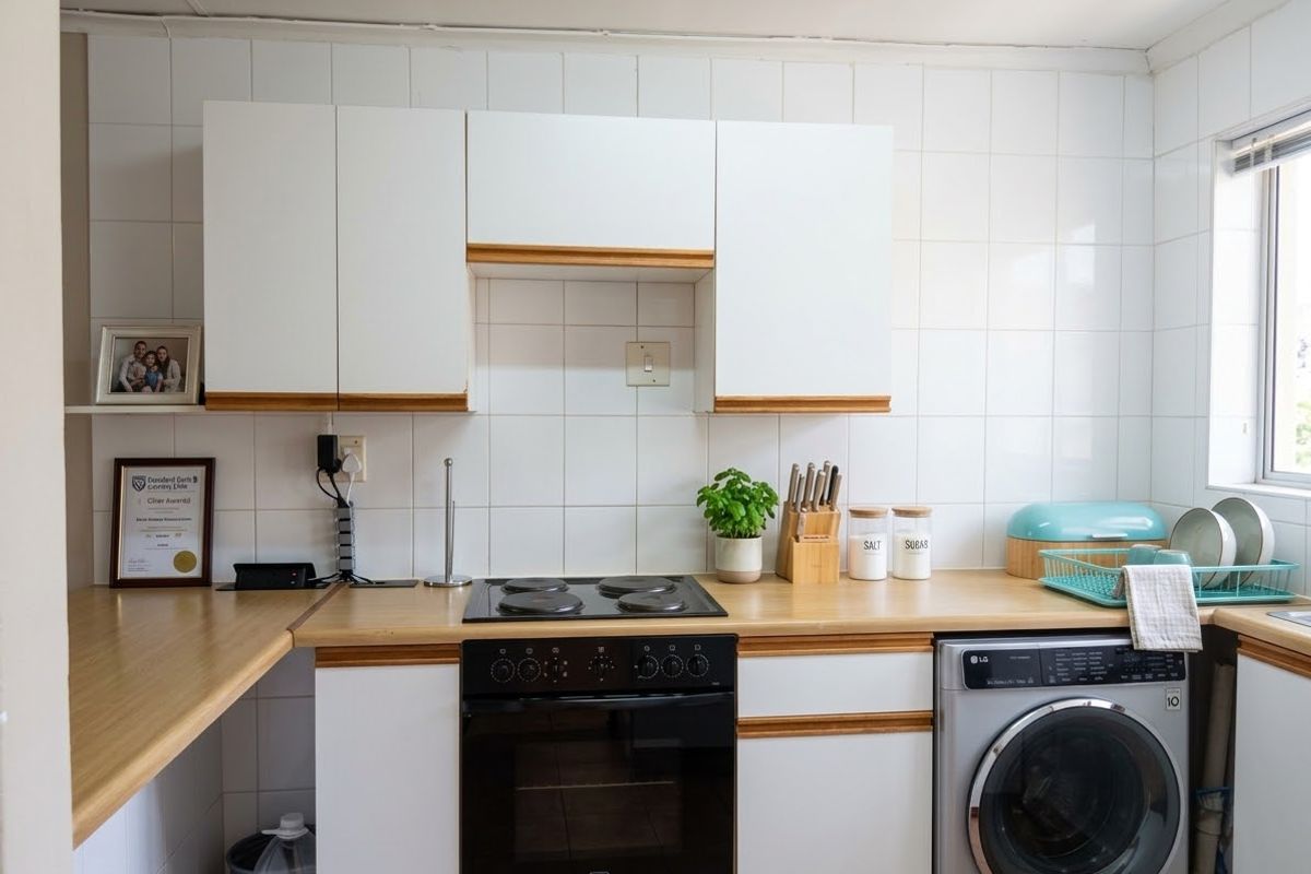 A functional kitchen featuring white cabinetry with wood trim, a laminate countertop, built-in electric oven and hob, and an integrated washing machine.