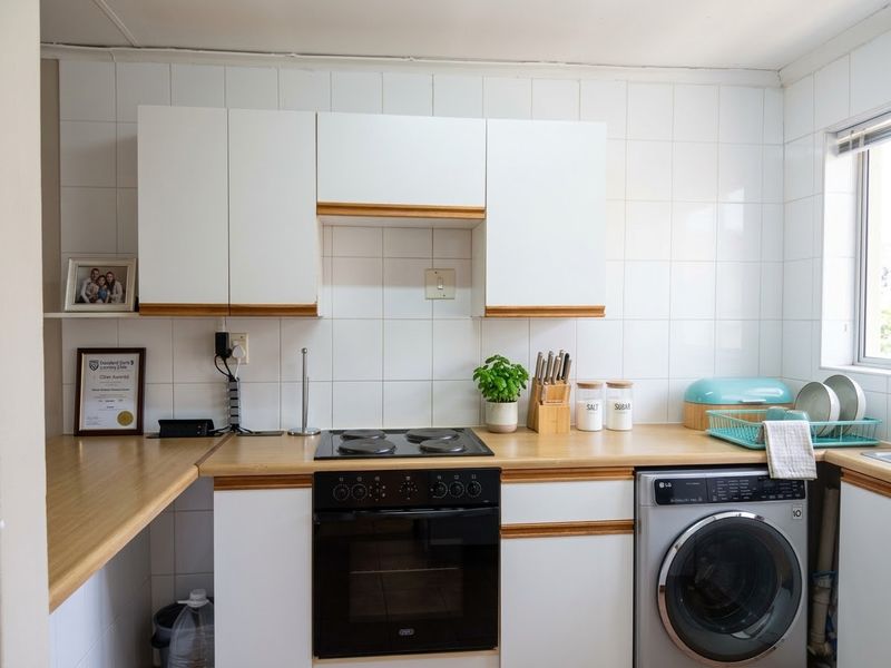 A functional kitchen featuring white cabinetry with wood trim, a laminate countertop, built-in electric oven and hob, and an integrated washing machine.
