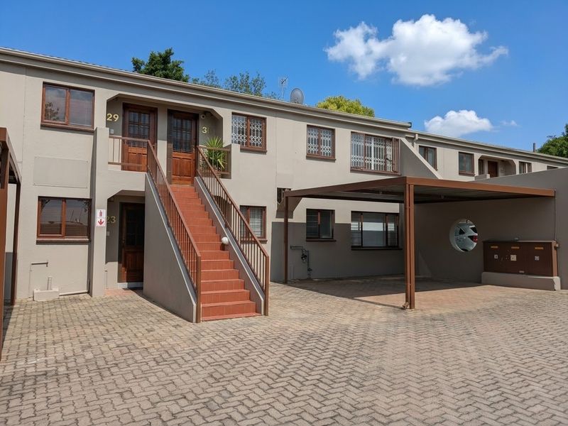 Front elevation of a multi-unit apartment complex featuring paved driveway, covered carport parking, and external staircase access to upper-level units.