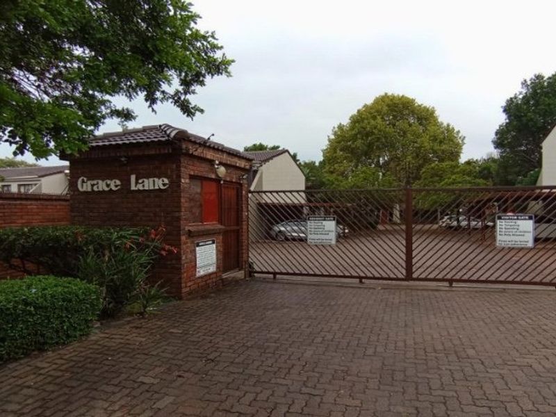 The entrance to Grace Lane apartment complex featuring a brick security guard house, metal security gate, and paved driveway access.