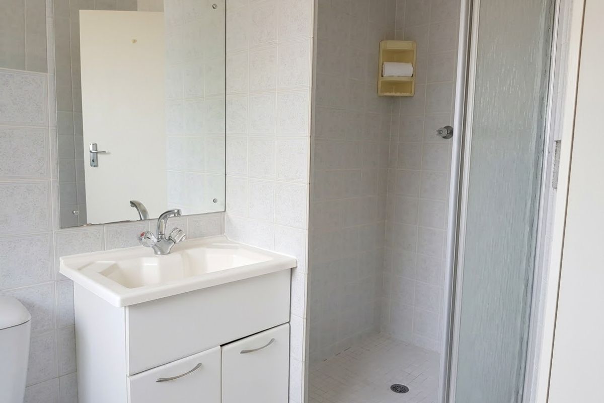 A functional bathroom featuring a vanity cabinet with basin, wall mirror, and a separate shower enclosure with tiled finishes.