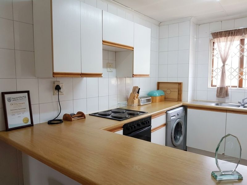 A functional kitchen featuring white cabinetry, laminate countertops, a built-in electric hob and oven, and tiled splashbacks with a window for natural light.