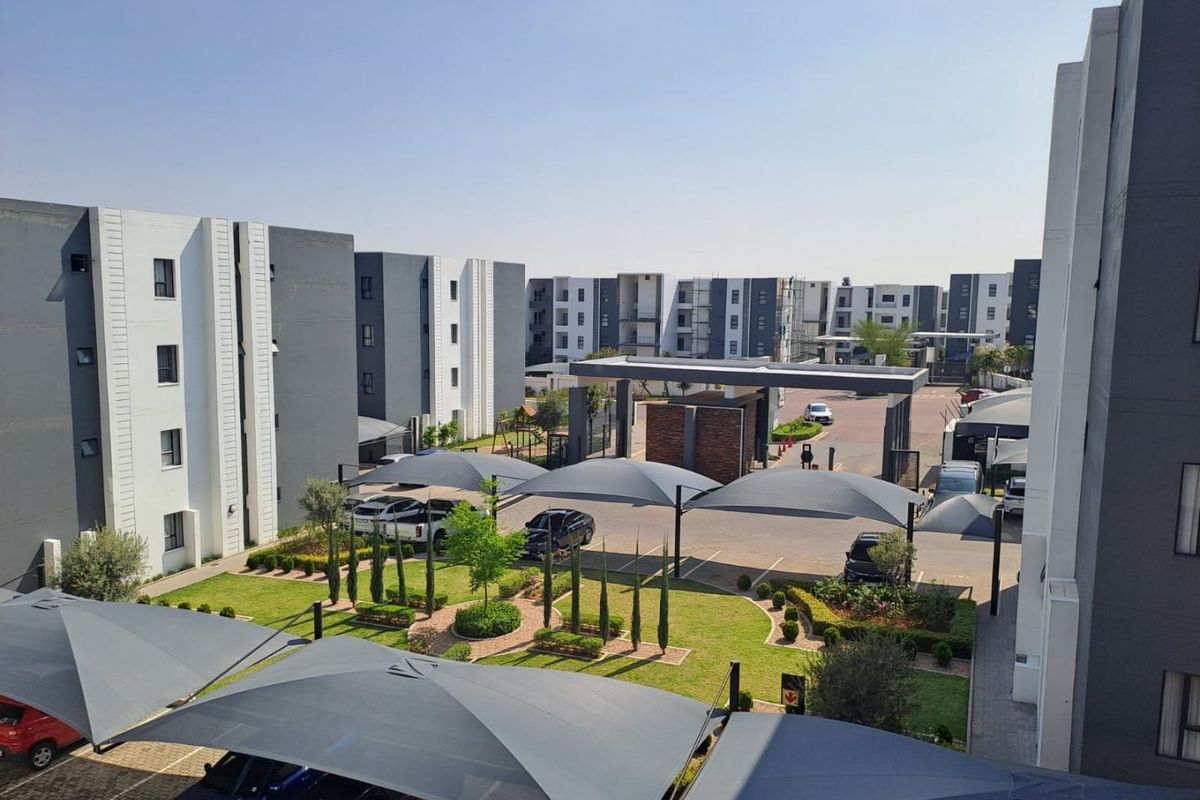 An elevated view of a modern apartment complex featuring landscaped gardens, paved parking areas with shade ports, and a secure gated entrance.