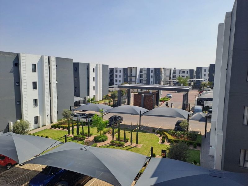 An elevated view of a modern apartment complex featuring landscaped gardens, paved parking areas with shade ports, and a secure gated entrance.