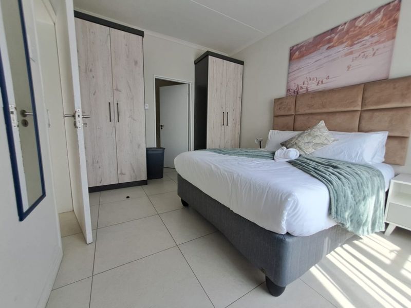 A well-maintained bedroom featuring neutral tiled flooring, built-in storage cupboards, and a modern upholstered headboard.