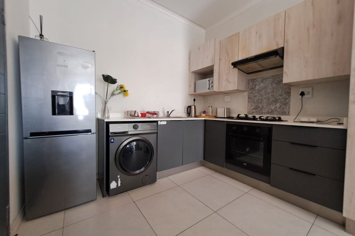 Modern kitchen featuring two-tone cabinetry, stone countertops, built-in oven, gas hob, extractor fan, and tiled flooring.