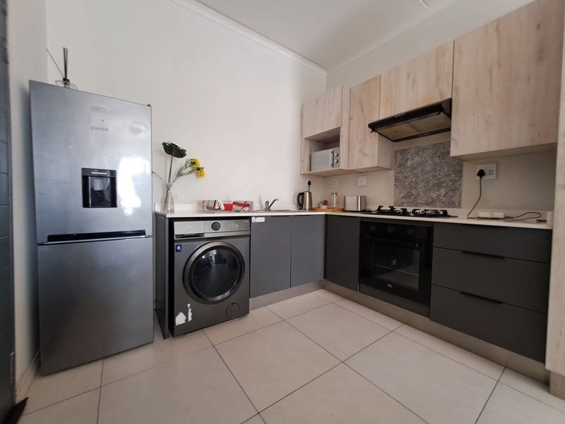 Modern kitchen featuring two-tone cabinetry, stone countertops, built-in oven, gas hob, extractor fan, and tiled flooring.