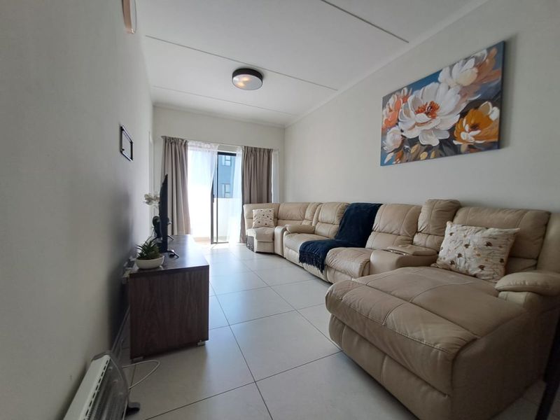 A bright living room featuring neutral tiled flooring and a sliding glass door providing access to an outdoor area.