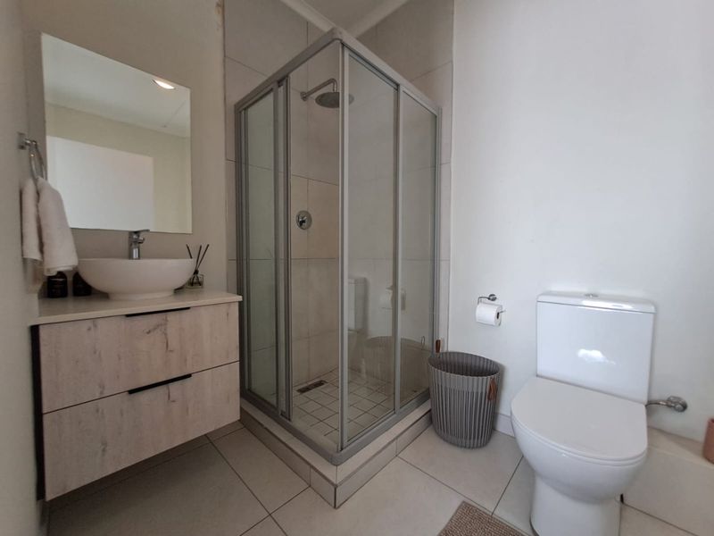 Modern bathroom featuring a floating vanity with a vessel sink, a corner shower enclosure, and a standard toilet with neutral floor tiling.