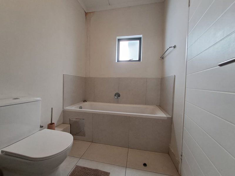 A functional bathroom featuring a built-in bathtub, toilet, and neutral floor-to-wall tiling, requiring minor maintenance to address ceiling water staining.