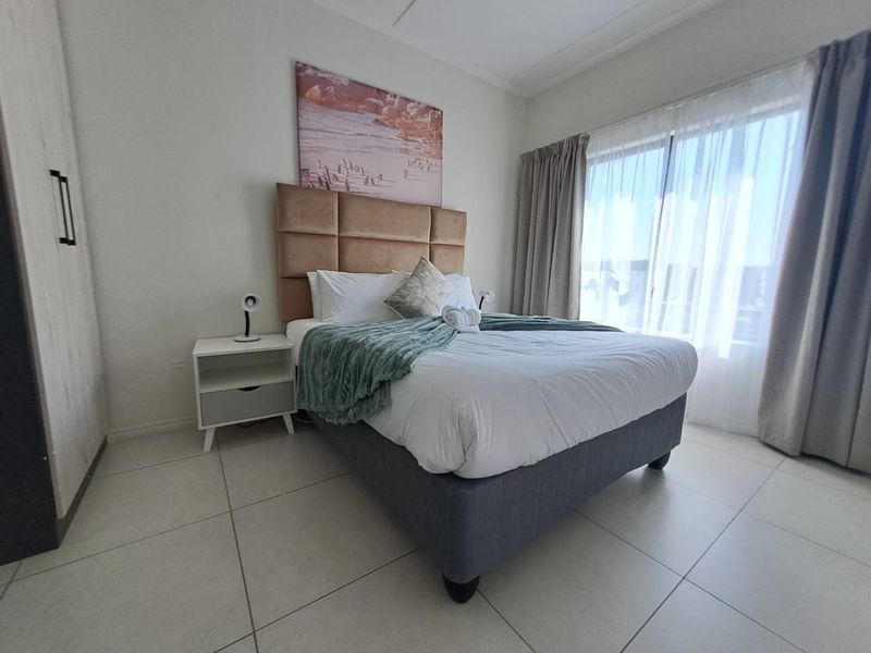A well-maintained bedroom featuring tiled flooring, a built-in wardrobe, and a sliding glass door providing natural light.