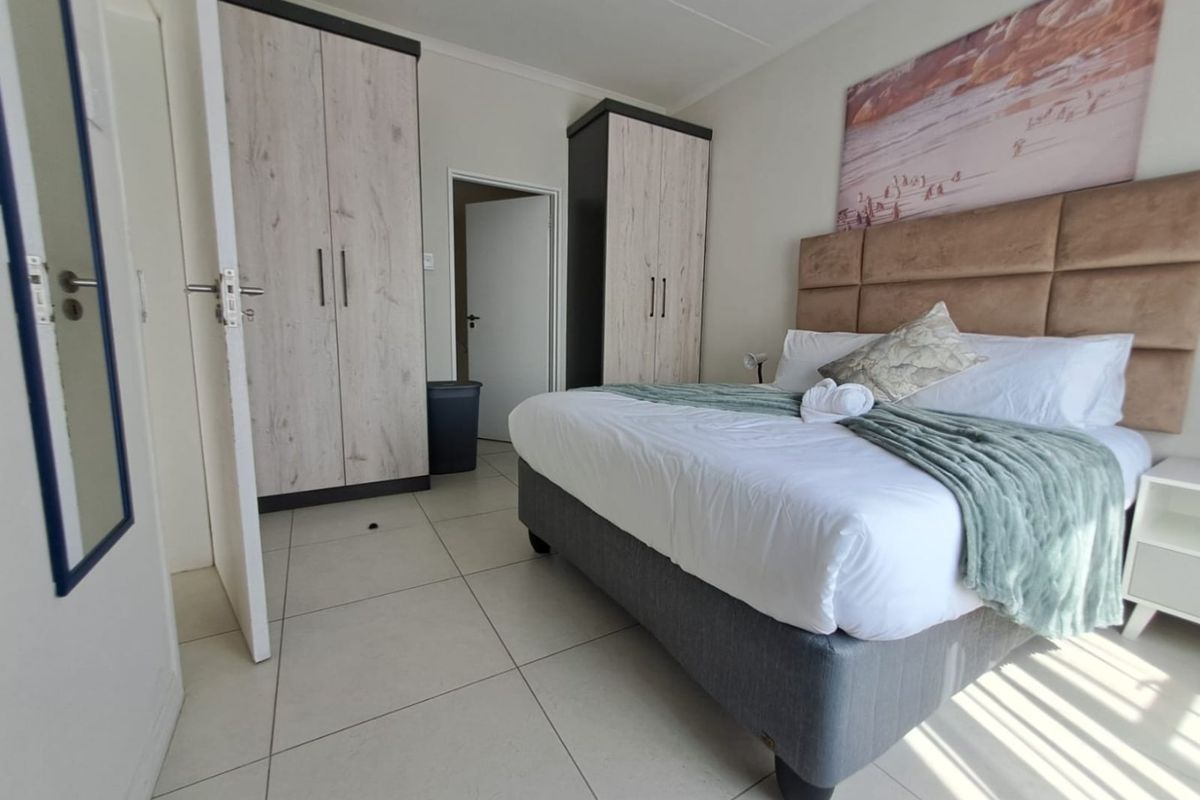 A well-maintained bedroom featuring neutral tiled flooring, built-in storage cupboards, and a modern upholstered headboard.