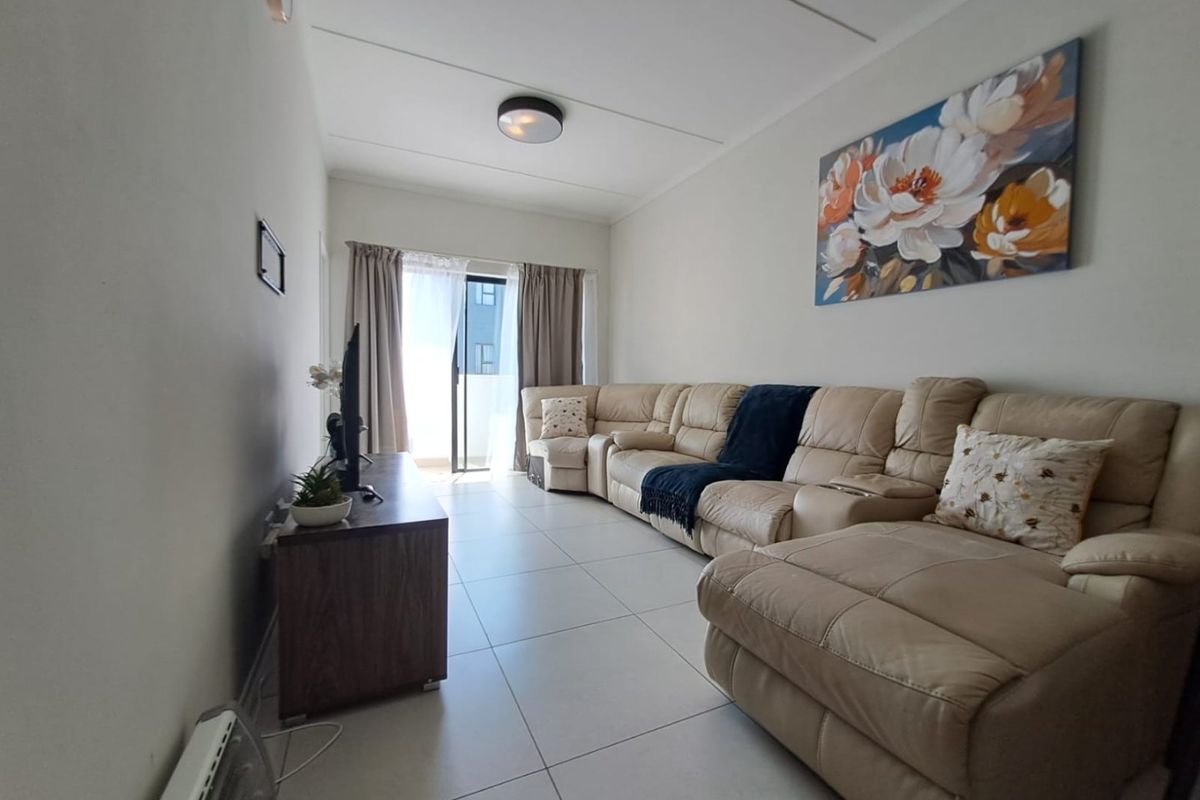A bright living room featuring neutral tiled flooring and a sliding glass door providing access to an outdoor area.