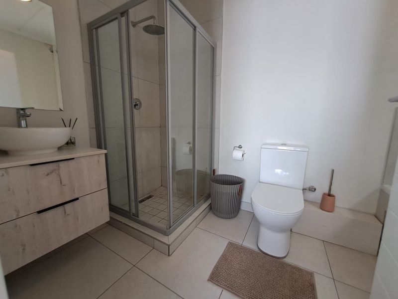 A modern bathroom featuring a glass-enclosed shower, a contemporary vanity with a vessel sink, and a standard toilet with tiled flooring.