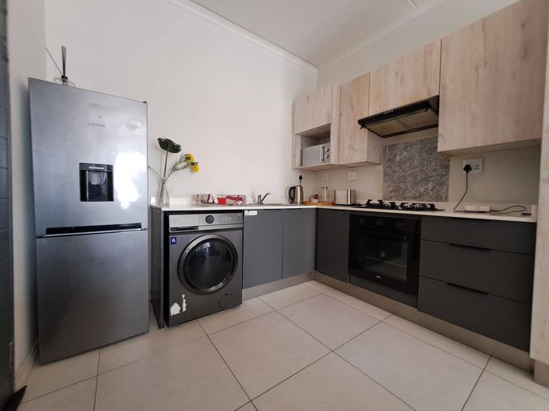Modern kitchen featuring two-tone cabinetry, stone countertops, built-in oven, gas hob, extractor fan, and tiled flooring with integrated laundry plumbing.