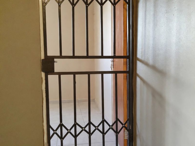 A view through a metal security gate into an empty hallway with tiled flooring and a wooden internal door.