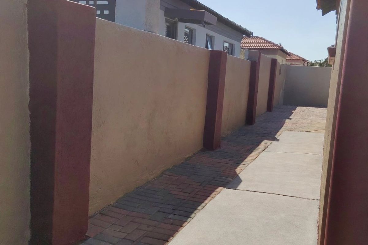A side walkway featuring a paved path, concrete sections, and a boundary wall with decorative columns.