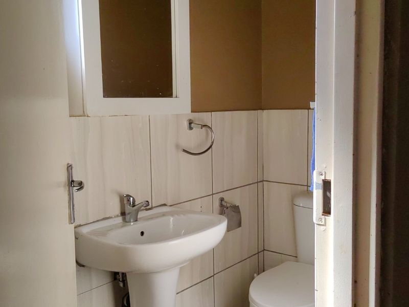 A compact bathroom featuring a white pedestal basin, toilet, and tiled finishes, offering a functional space ready for cosmetic updates.