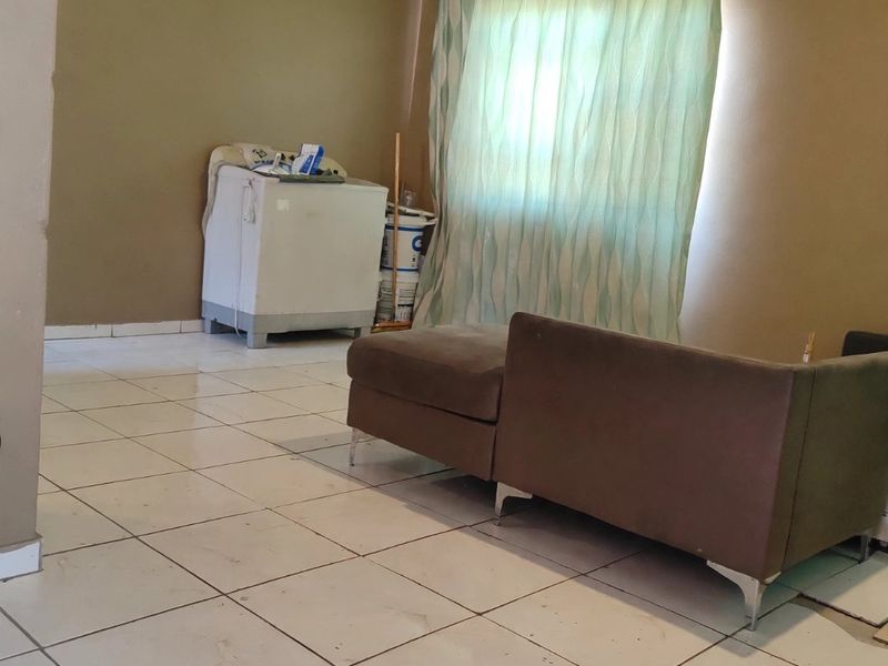 A living room area featuring tiled flooring and coved ceilings, currently showing signs of wear and requiring maintenance on the floor finishes.