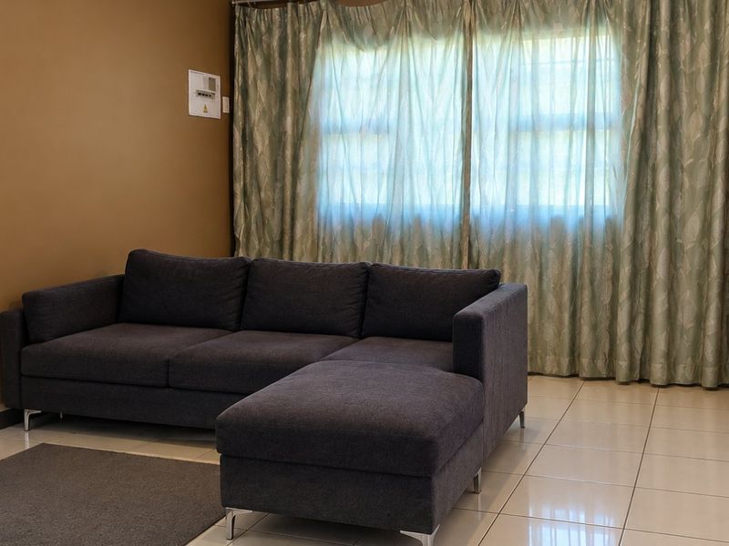 A living room featuring neutral tiled flooring and a wall-mounted electrical distribution board, providing a functional and well-lit space.