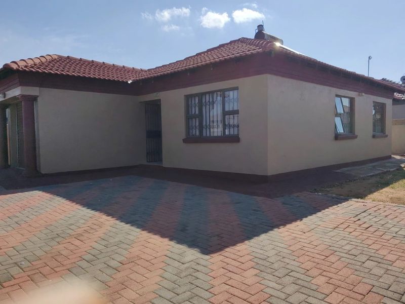 Front view of a single-story house featuring a tiled roof, solar geyser, and a paved driveway with secure window bars.