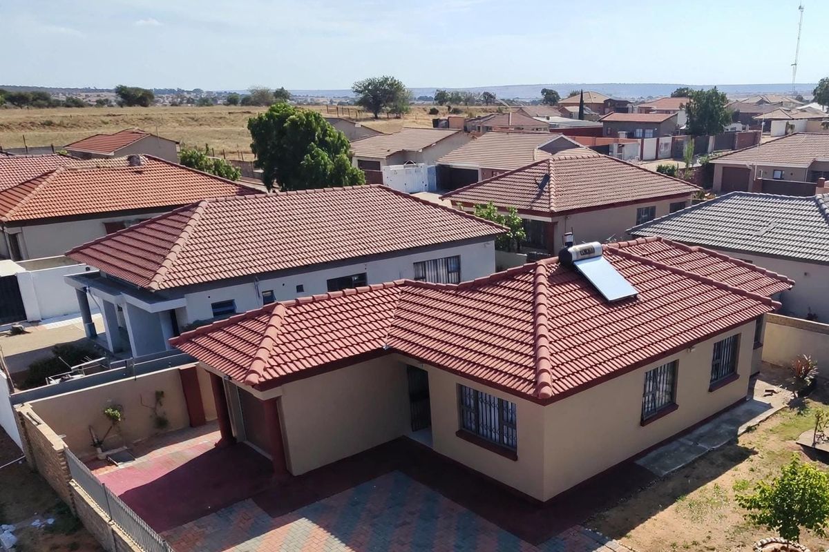 Aerial view of a residential property featuring a tiled roof, solar water heating system, and a paved driveway within a suburban neighborhood.
