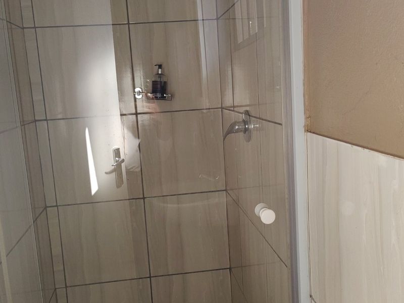 A functional shower enclosure featuring neutral wall tiles and a tiled floor, ready for a modern update.