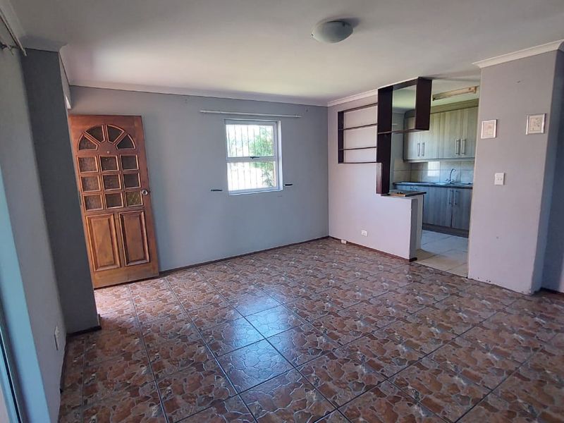 An open-plan living area featuring tiled flooring, a timber entrance door, and an adjacent kitchen with built-in cabinetry and sink.