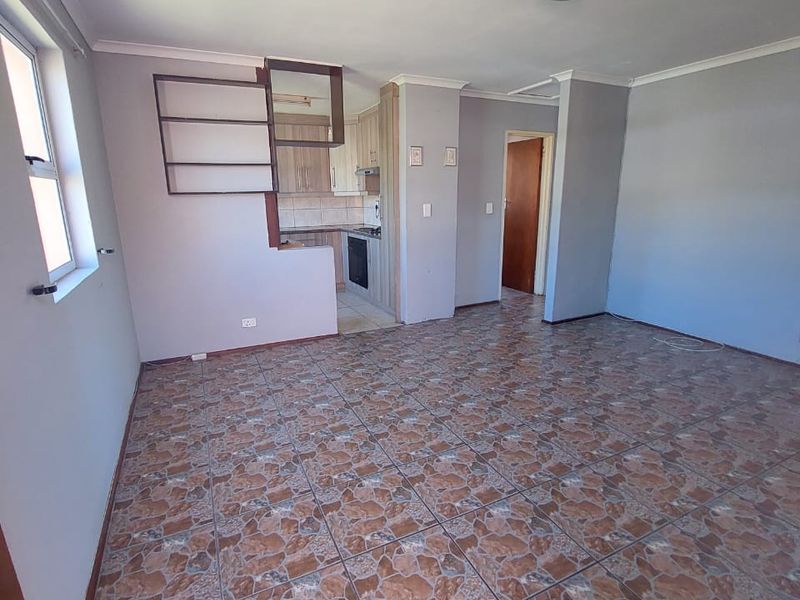 An open-plan living area featuring tiled flooring and a compact, integrated kitchen with built-in cabinetry, oven, and hob.