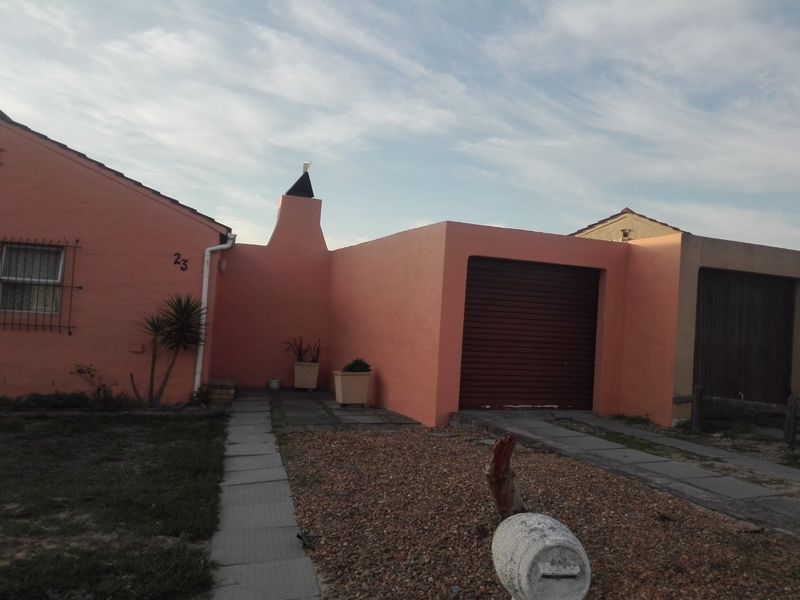 Front elevation of a single-story house featuring a roller garage door, chimney, and paved walkway access.