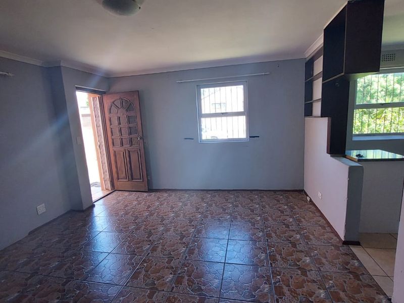 An open-plan living area featuring tiled flooring, built-in shelving, and security bars on the windows, offering a blank canvas for renovation.