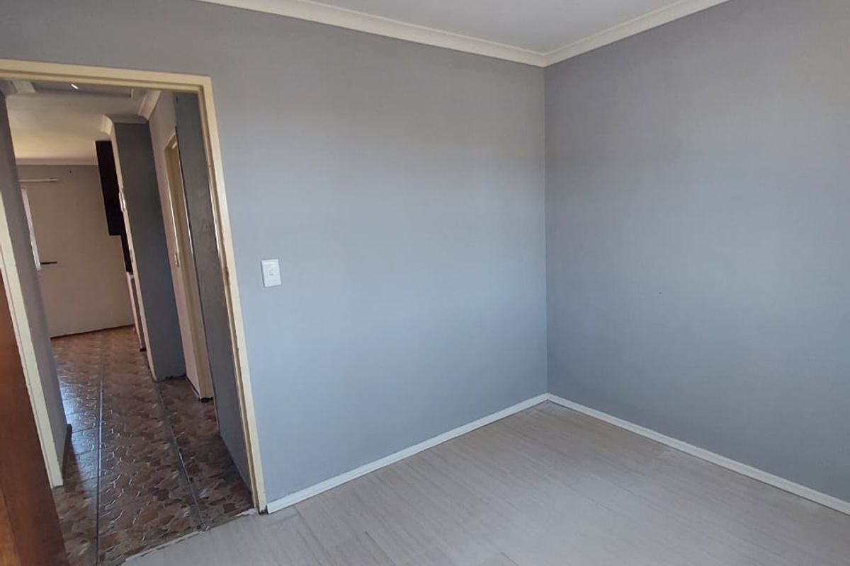 An empty bedroom featuring light-toned flooring, grey walls, and cove cornicing, with a doorway leading to an adjacent tiled hallway.