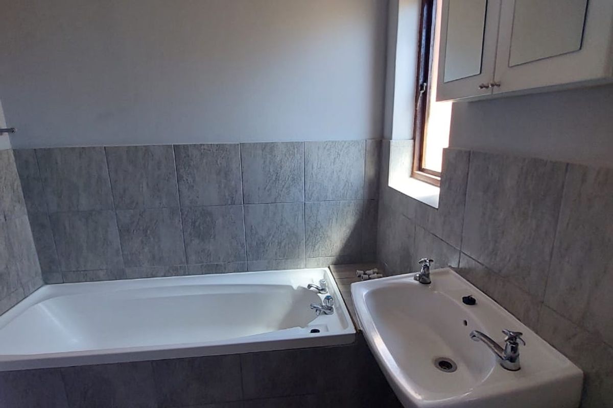 A functional bathroom featuring a built-in bathtub, wall-mounted basin, and neutral tiled finishes, offering a clean and practical space.