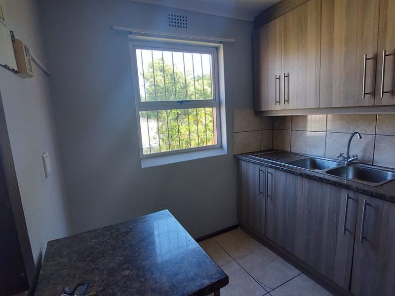 A functional kitchen featuring wood-look laminate cabinetry, granite-effect countertops, a double stainless steel sink, and tiled flooring.