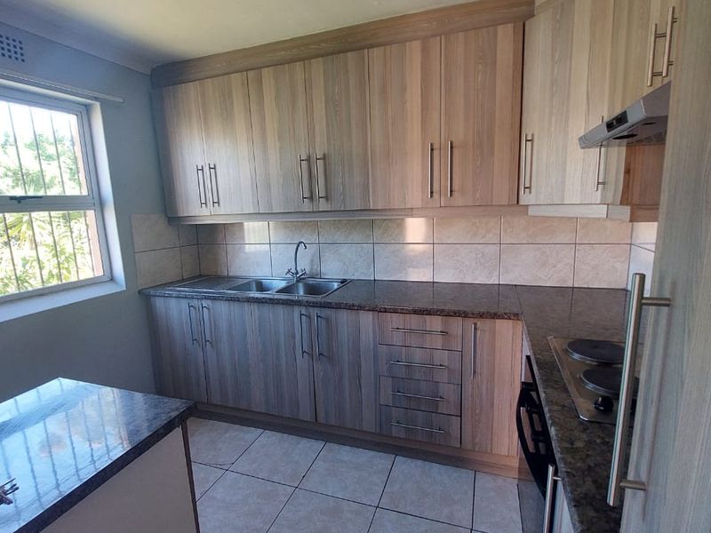 A functional kitchen featuring wood-look laminate cabinetry, granite countertops, tiled flooring, and built-in cooking appliances, offering a clean and practical workspace.