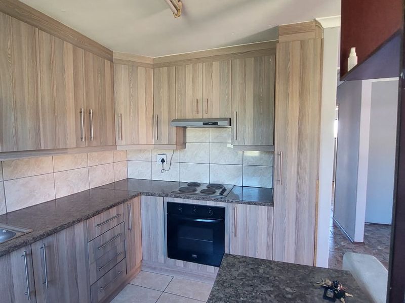 A functional kitchen featuring wood-look laminate cabinetry, granite countertops, built-in oven, electric hob, and tiled flooring.