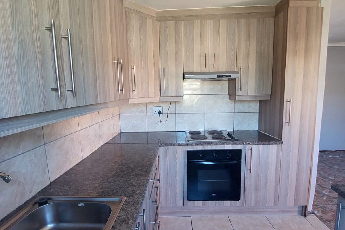 A functional kitchen featuring light wood-look cabinetry, granite-style countertops, built-in oven, hob, and extractor fan with neutral ceramic tiling throughout.