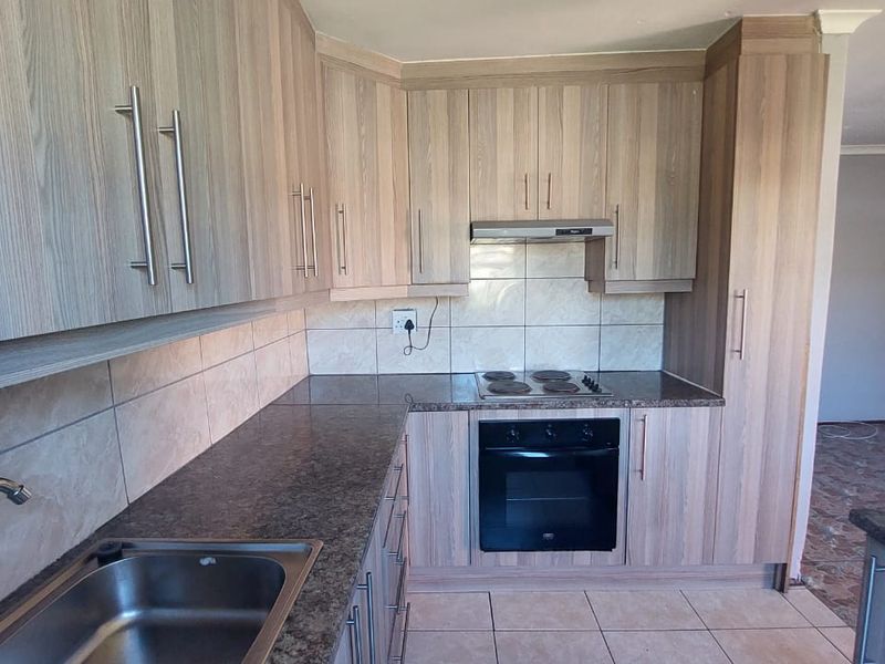 A functional kitchen featuring light wood-look cabinetry, granite-style countertops, built-in oven, hob, and extractor fan with neutral ceramic tiling throughout.