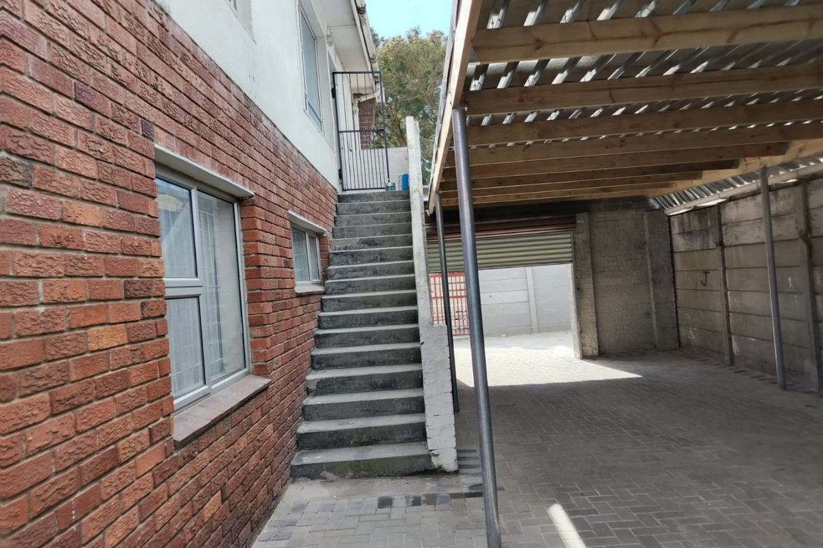 Rear exterior view featuring a brick facade, concrete staircase leading to an upper level, and a covered carport area with paved flooring.