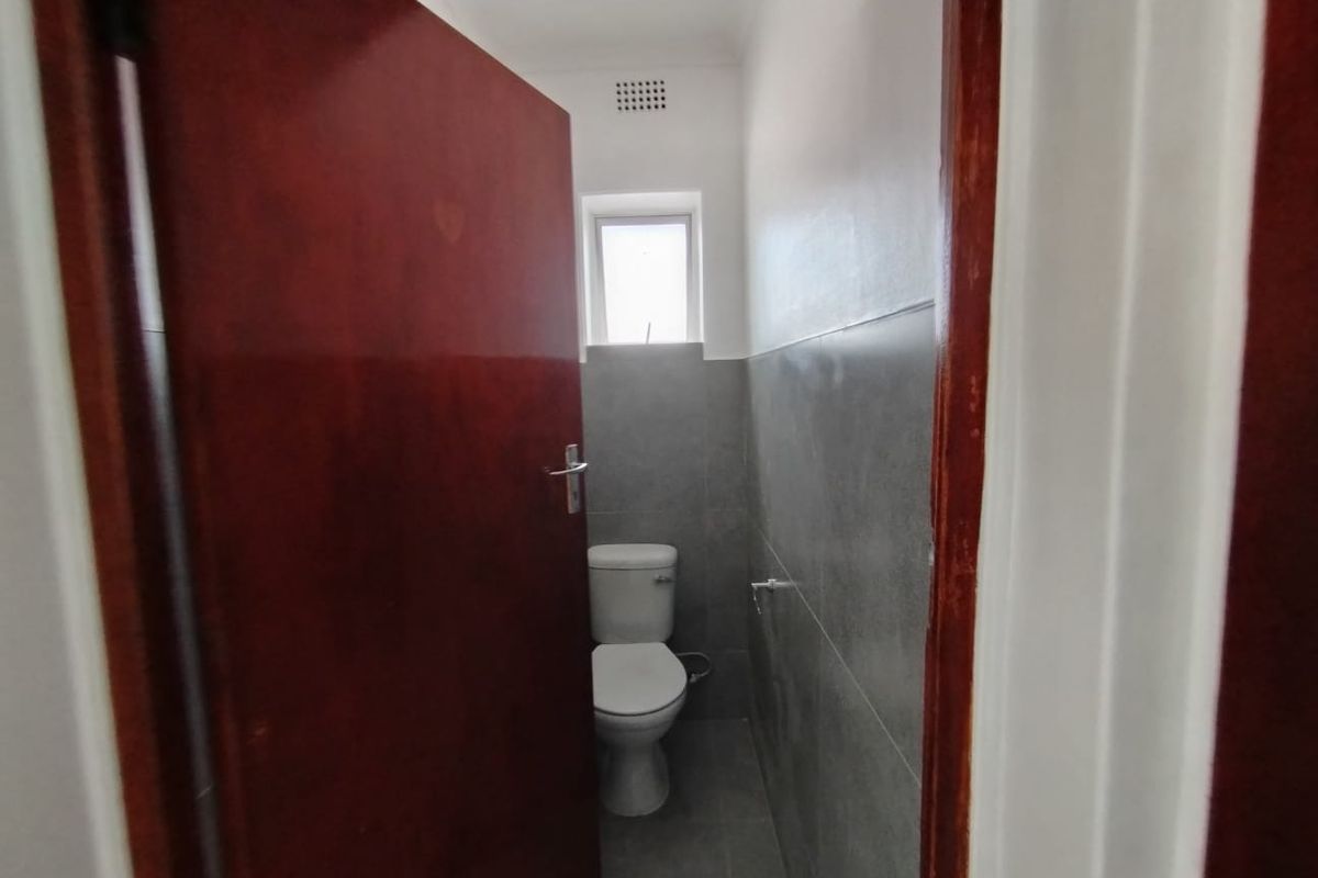 A compact, clean bathroom featuring modern grey wall and floor tiles, a white toilet, and a small window for natural light.