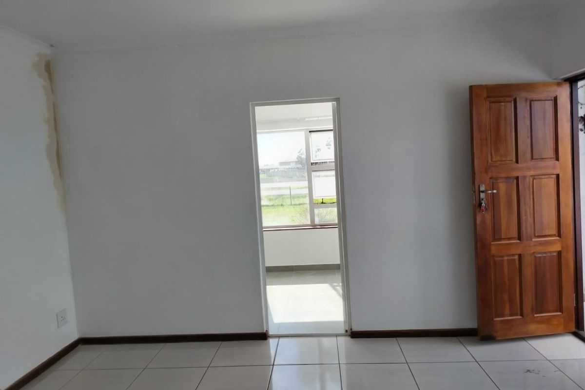 An empty bedroom featuring tiled flooring and a timber door, with visible water staining on the wall requiring attention.