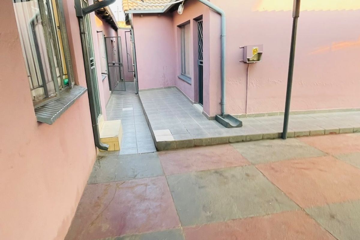 A paved rear courtyard area featuring a covered patio section, security gates, and external building infrastructure.
